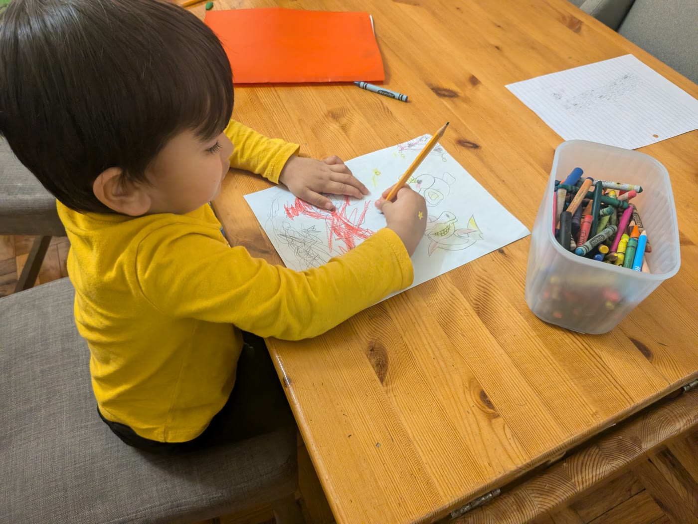 Eham, age 3, drawing with a pencil at the kitchen table